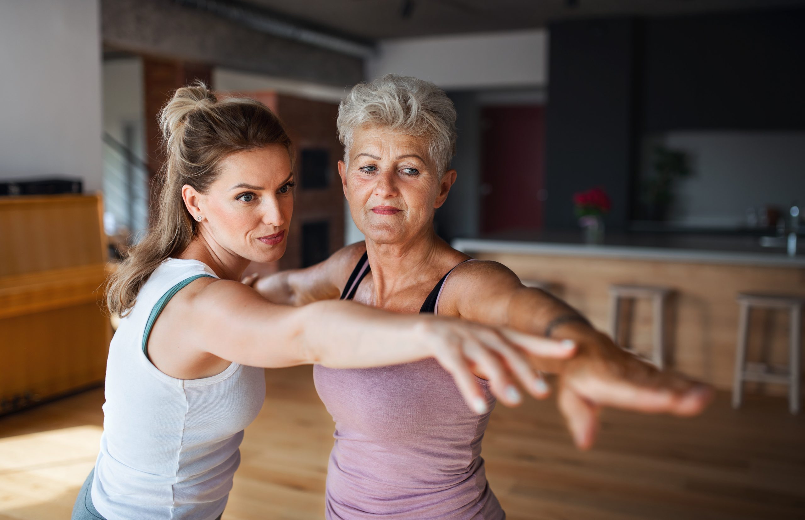 Active Senior Woman In Sportsclothes Exercising With Her Adult Daughter Indoors At Home.