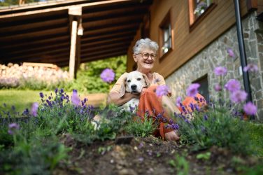 Portrait Of Senior Woman Sitting Outdoors In Garden, Pet Dog Friendship.